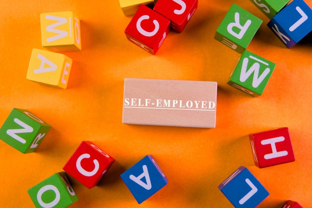 colorful,letter,blocks,surround,a,wooden,sign,that,reads,self employed